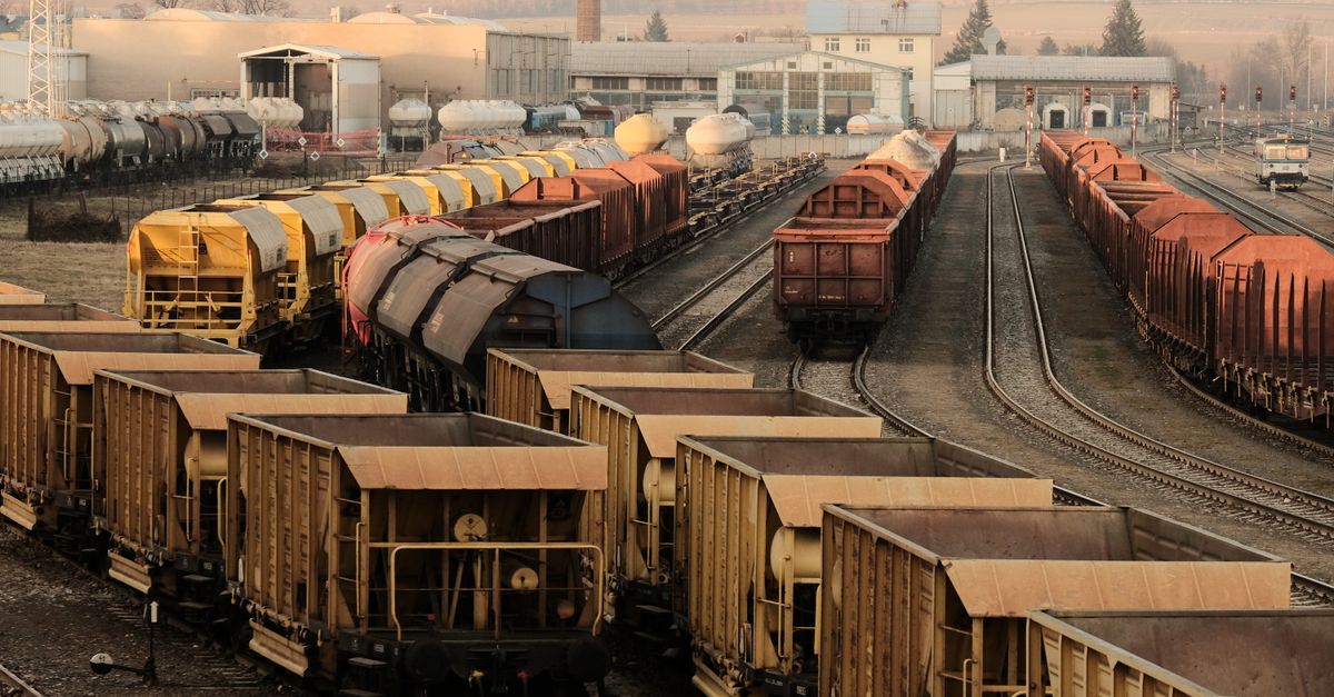 A busy freight train yard with multiple tracks and a variety of train cars in a rural setting.